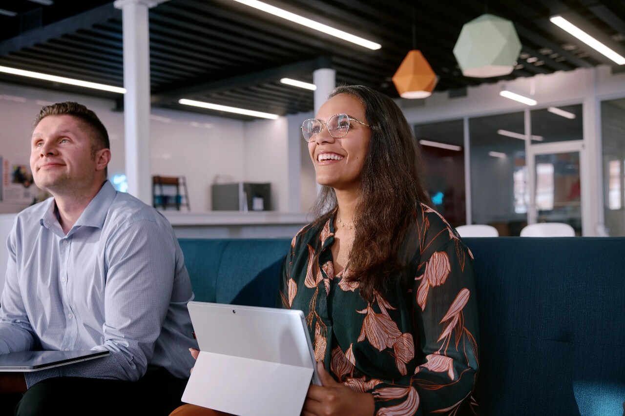 Eine lächelnde Frau, die mit einem aufgeklappten Laptop hinter einem Tresen sitzt.